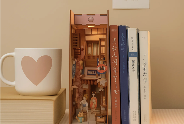 Book Nook en forma de cafetería iluminada colocado entre libros en una estantería; una pequeña escena en miniatura con mesa, silla y decoración detallada que muestra cómo estas maquetas en miniatura pueden fomentar la creatividad y concentración en el aprendizaje