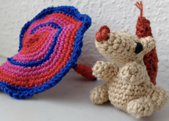 Pequeño muñeco tejido de amigurumi junto a una pieza circular de crochet colorida, mostrando el resultado final de la técnica artesanal con hilos de algodón y puntadas en espiral